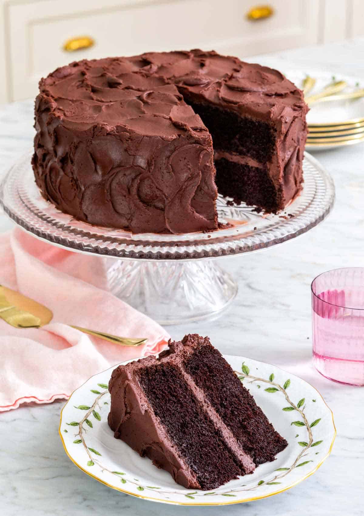 A cake stand with devil's food cake with a slice cut and served in front.