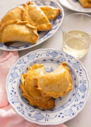 A plate with two empanadas by a plate with more.