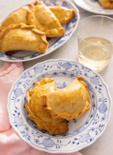 A plate with two empanadas by a plate with more.