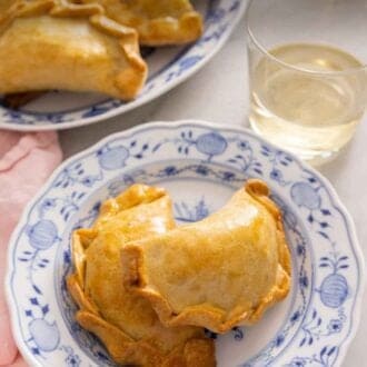 Pinterest graphic of a plate of two empanadas by a platter of more empanadas.