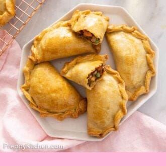 Pinterest graphic of a platter of empanadas with one cut open.