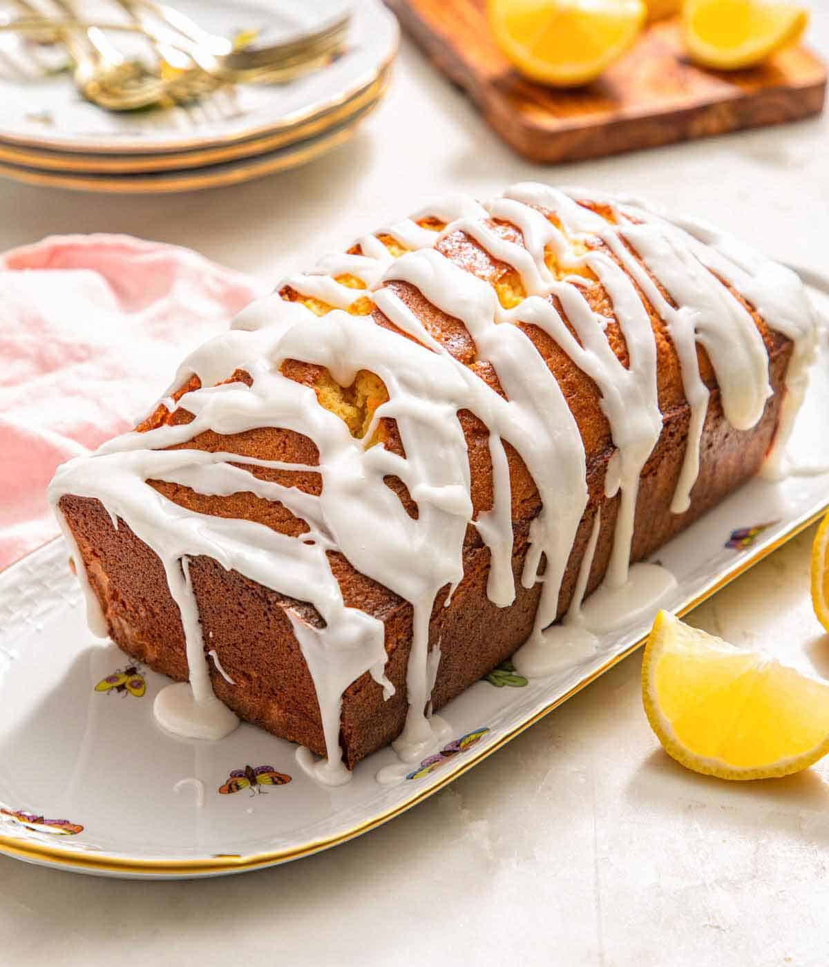 Pinterest graphic of a loaf of lemon pound cake with glaze drizzled over top with lemon wedges around it.