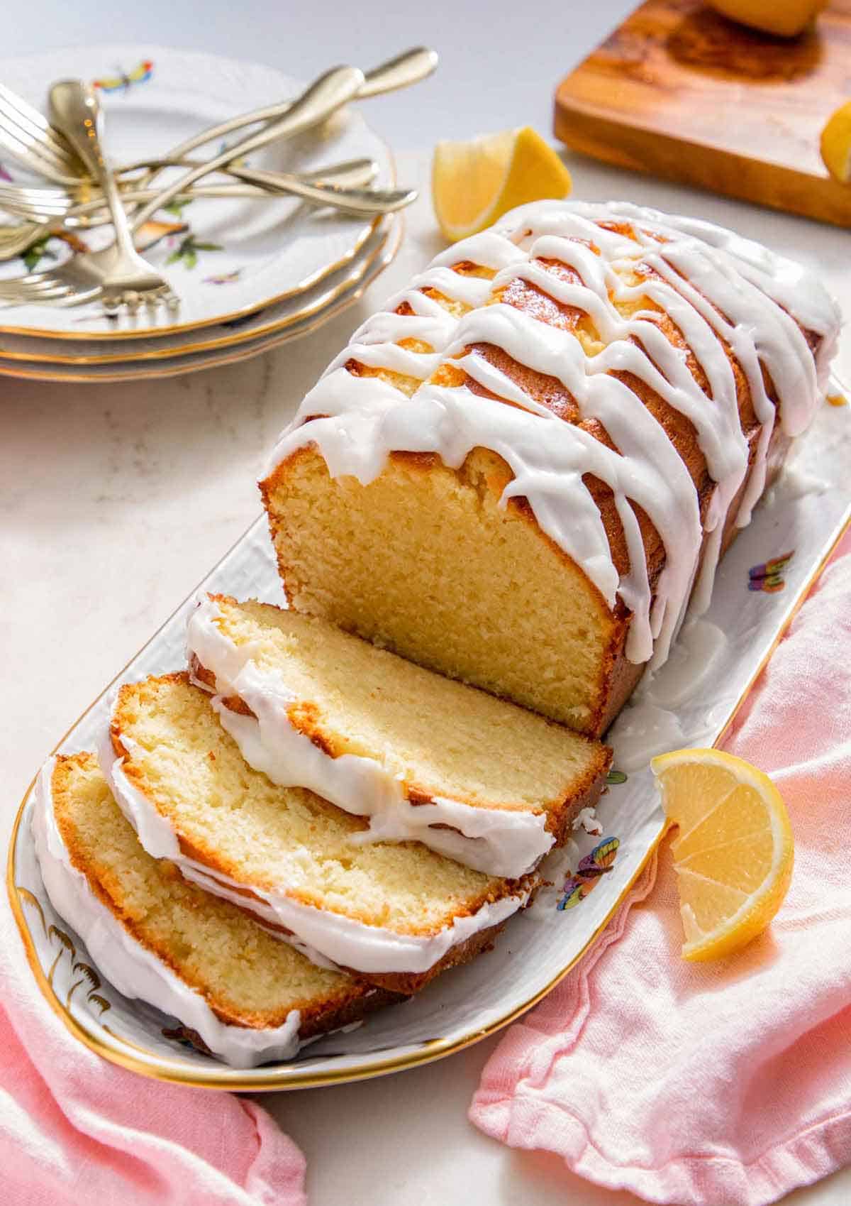 A platter with a loaf of lemon pound cake with three slices cut.