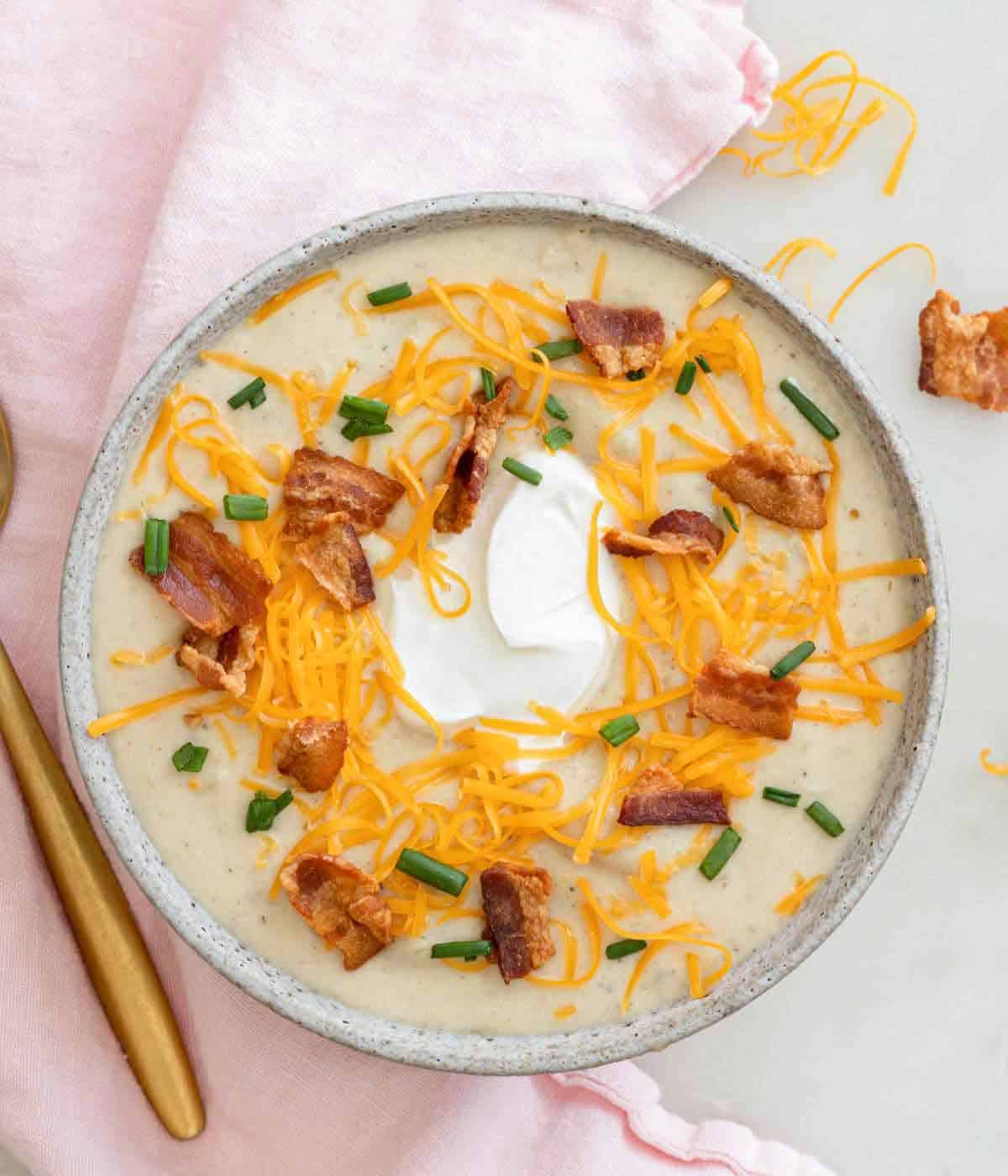 Overhead view of a bowl of potato soup with bacon, cheese, sour cream, and chives.