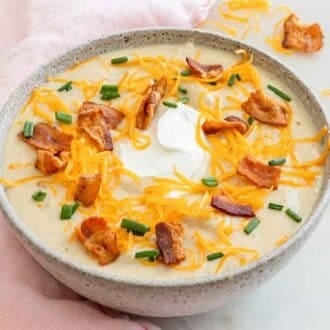 A bowl of potato soup with toppings on the counter and soup.