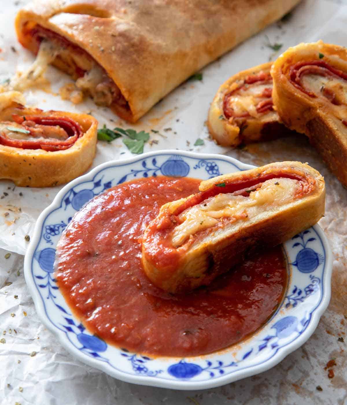 A plate of pizza sauce with a piece of stromboli dipped in and more surrounding it.