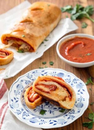 Two pieces of stromboli on a plate by some sauce and the rest of the stromboli.