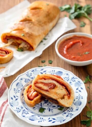 Two pieces of stromboli on a plate by some sauce and the rest of the stromboli.