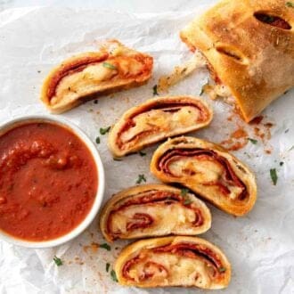 A log of stromboli with five pieces cut, by a bowl of sauce.