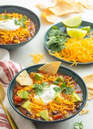 Two bowls of taco soup with a plate of toppings on the side.