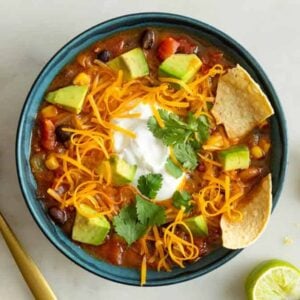 Overhead view of a bowl of taco soup with shredded cheese, chips, avocado, cilantro, and sour cream on top.