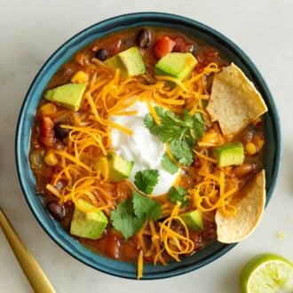 Overhead view of a bowl of taco soup with shredded cheese, chips, avocado, cilantro, and sour cream on top.