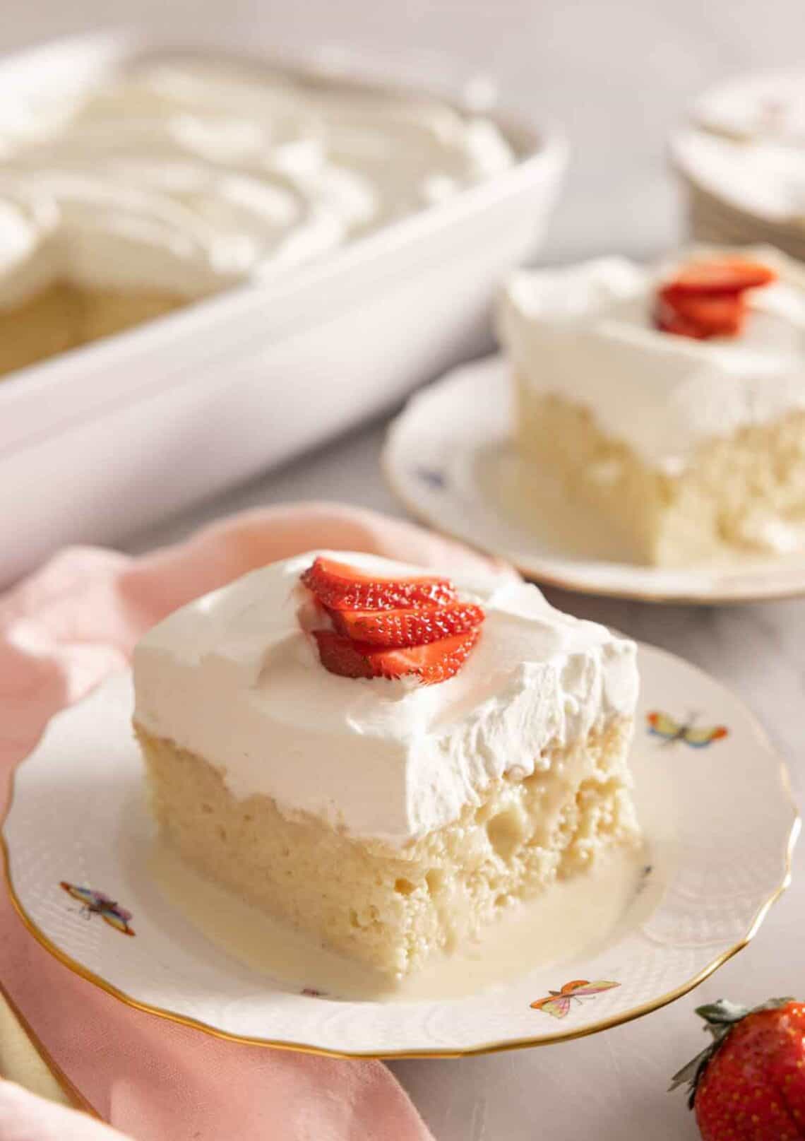 Two plates, one in front, with a square slice of tres leches cake.