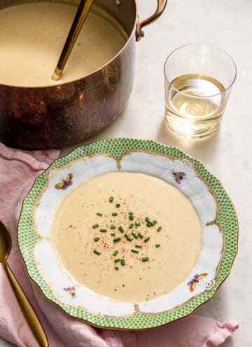 A bowl of vichyssoise with chives on top by a glass of wine and more soup.
