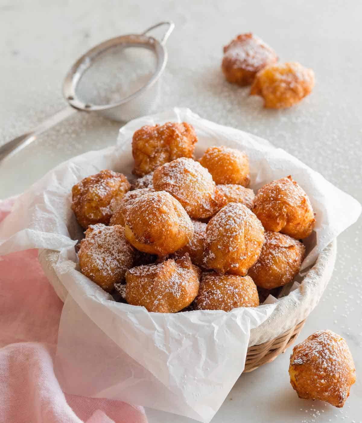 A basket lined with parchment with zeppole with powdered sugar dusted on top.