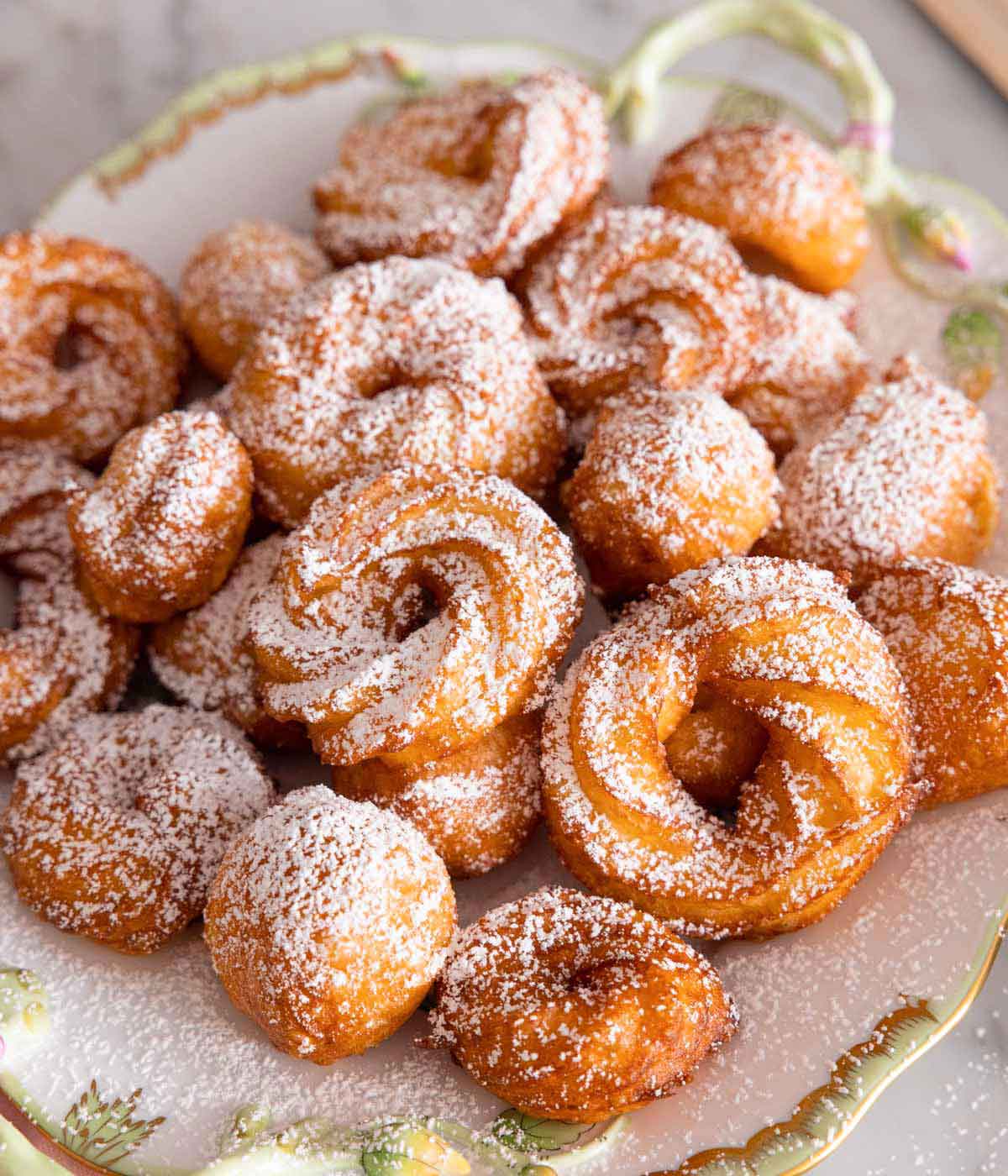 A plate with different sized zeppole with powdered sugar on top.