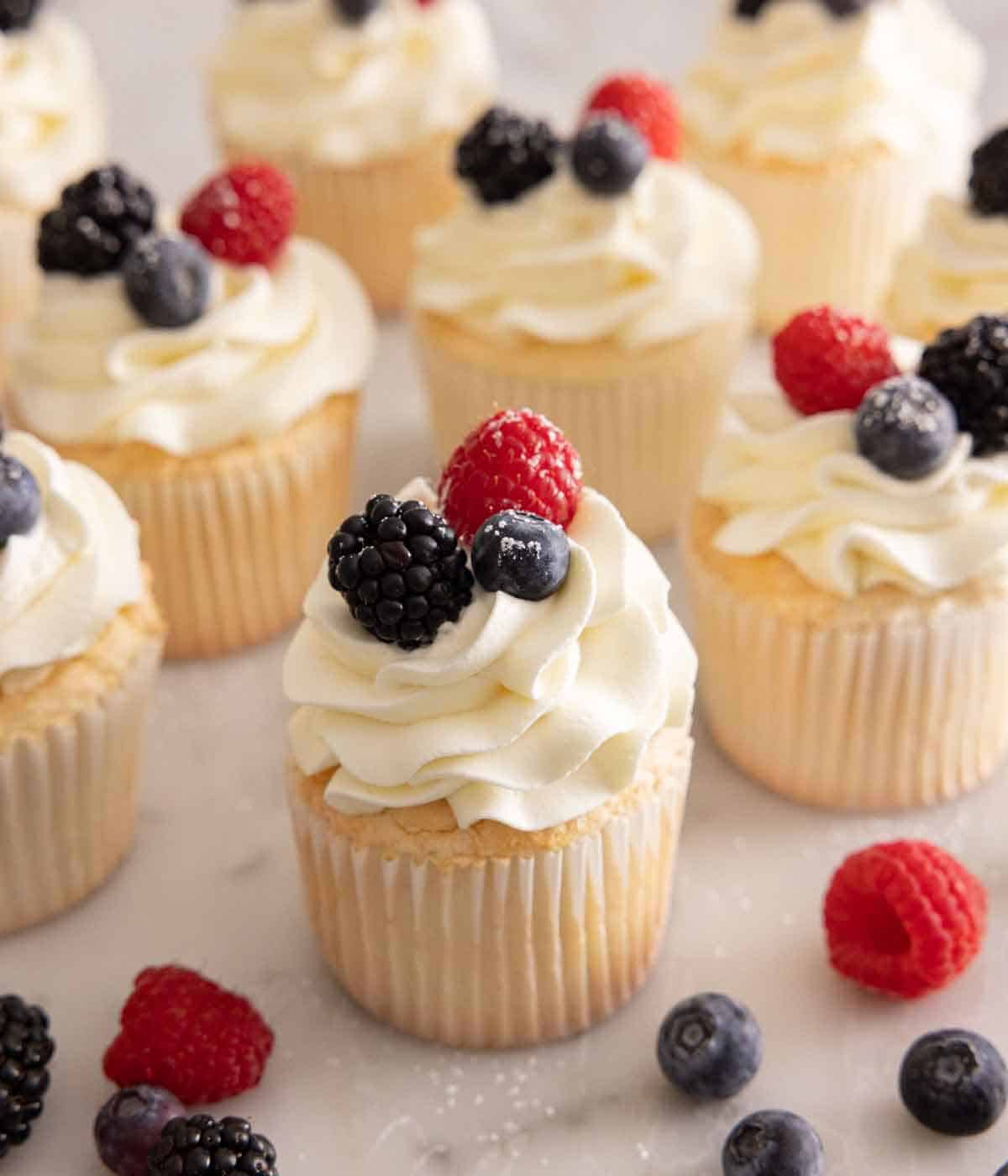 Multiple angel food cupcakes with berries on top.