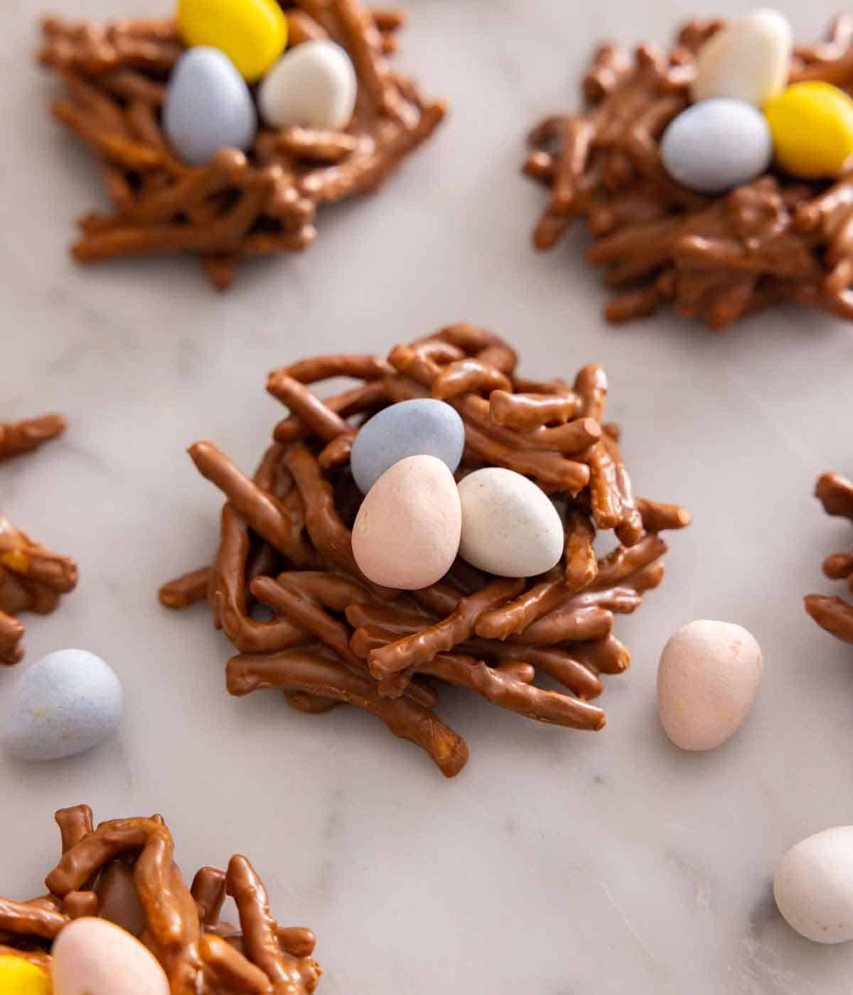 Multiple birds nest cookies with one in focus with candy eggs scattered around.