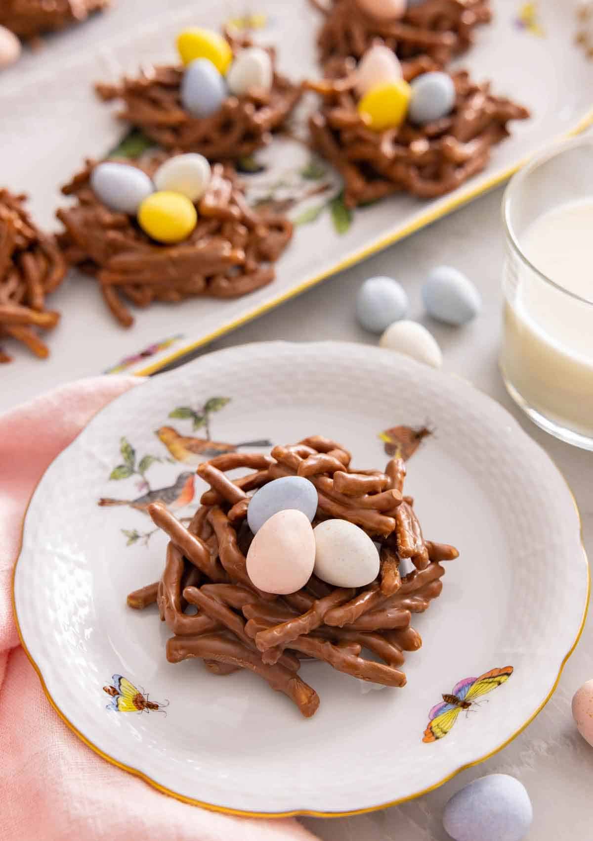 A plate with a birds nest cookie on it by a glass of milk.