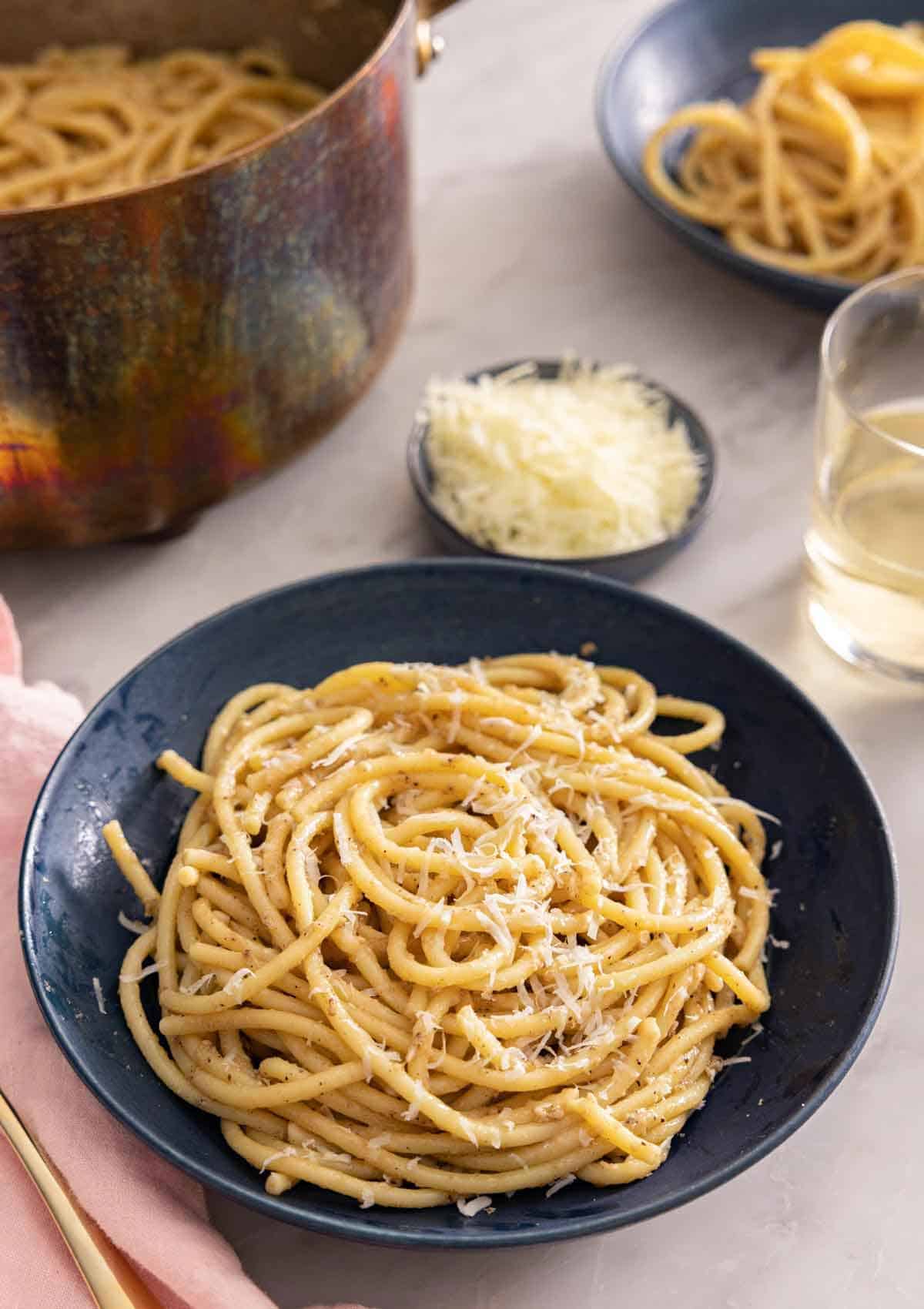 A plate with cacio e pepe with grated cheese and more noodles in the background.