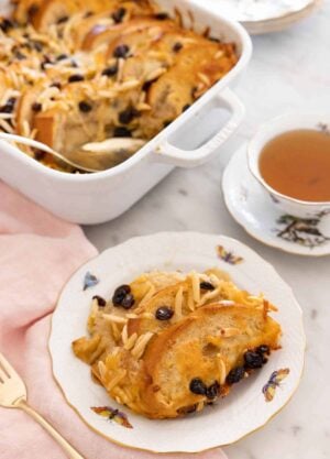 A plate with a serving of capirotada in front of a cup of tea and a baking dish.