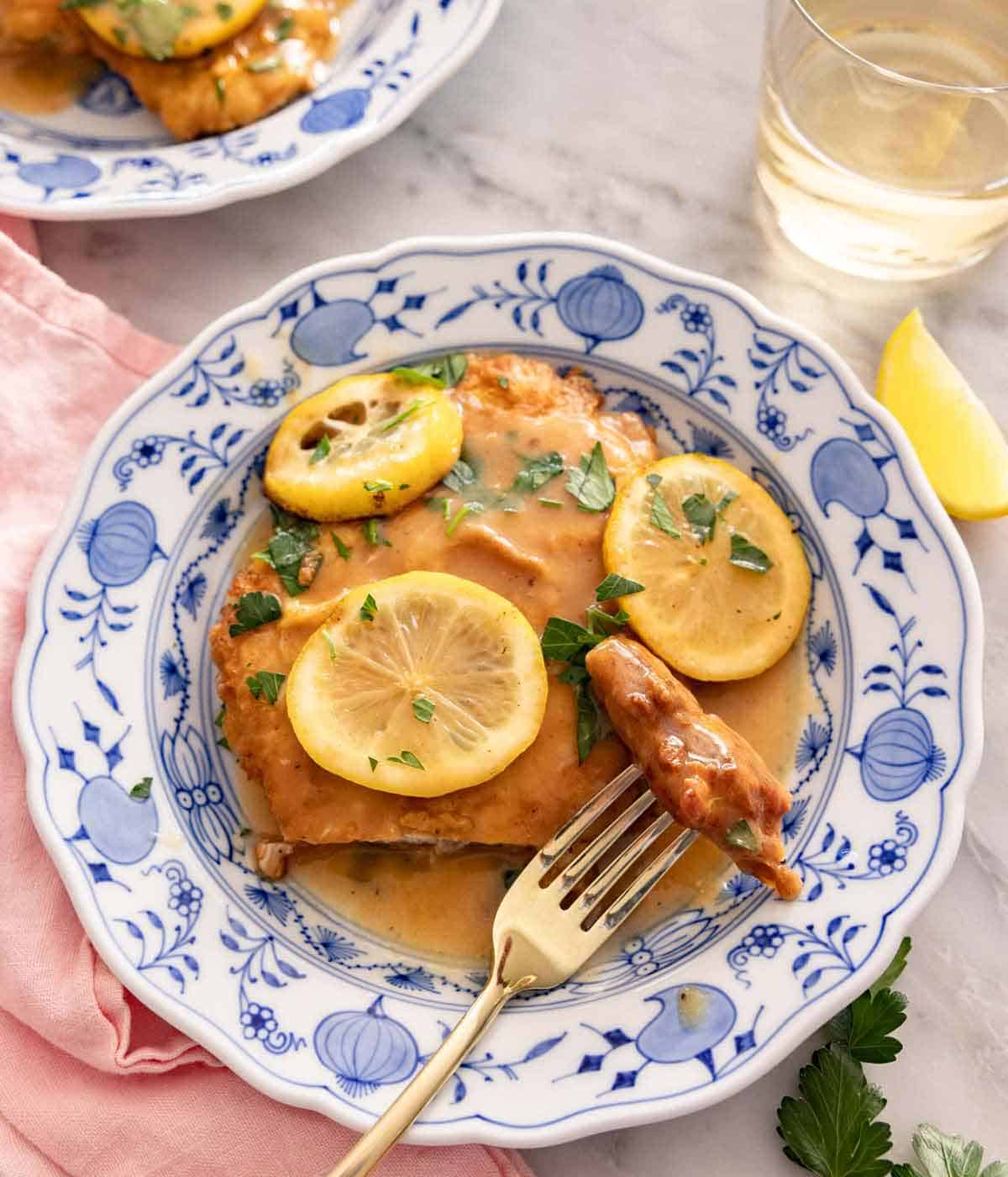 A plate of chicken Francese with a bite on a fork, with lemon slices on top.