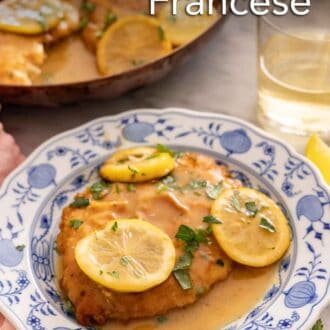 Pinterest graphic of a plate with chicken Francese with lemon slices on top by a glass of wine and skillet.