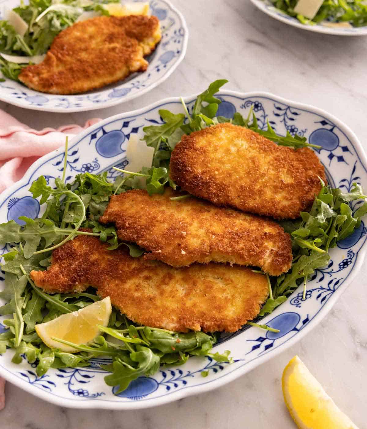 A platter of chicken Milanese over a bed of arugula.
