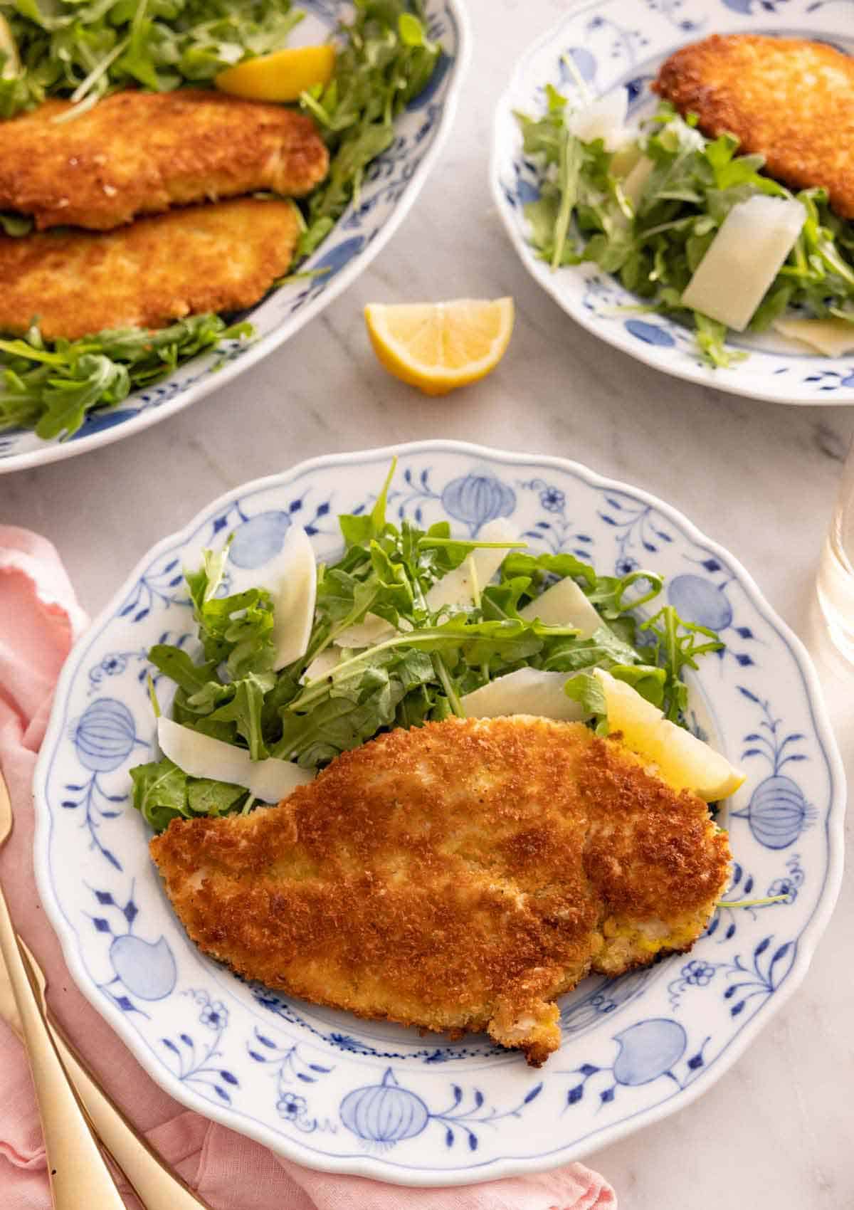 A plate with chicken Milanese alongside an arugula salad.