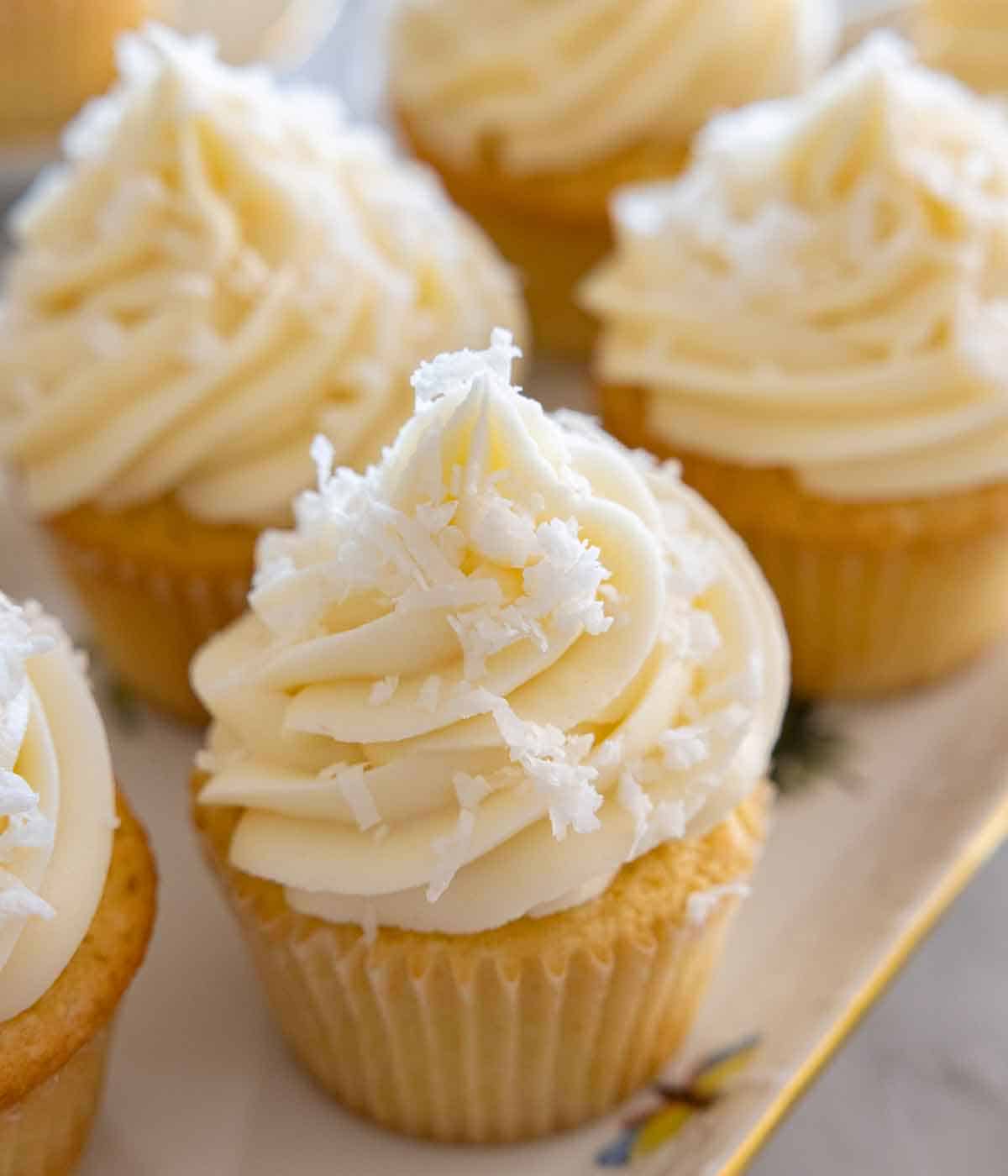 Close up of a coconut cupcake on a platter with multiple.
