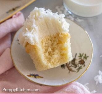 Pinterest graphic of a plate with a coconut cupcake with a bite taken out of it.
