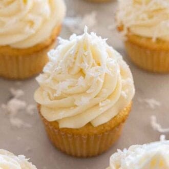 Multiple coconut cupcakes with frosting and shredded coconut on top.