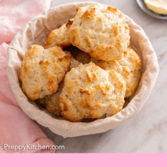 Pinterest graphic of a basket of drop biscuits with butter in the background.