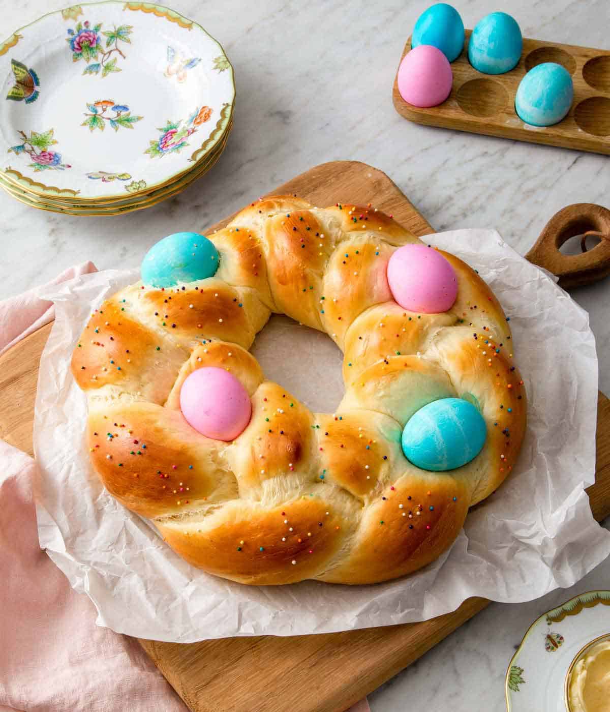 Easter bread on top of a parchment-lined wooden serving board with dyed eggs in the background.