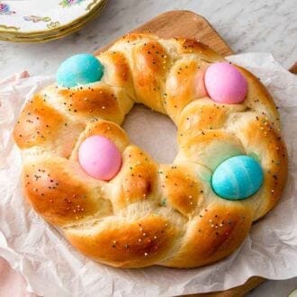 A parchment-lined board with an Easter bread on it with pink and blue eggs.