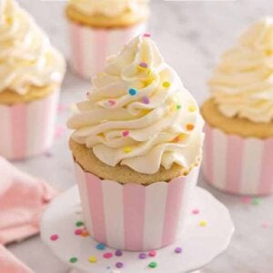 A cupcake on a mini stand with Italian buttercream piped on top. More cupcakes in the background.