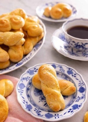 A plate with two koulourakia by a mug of coffee and a platter more.