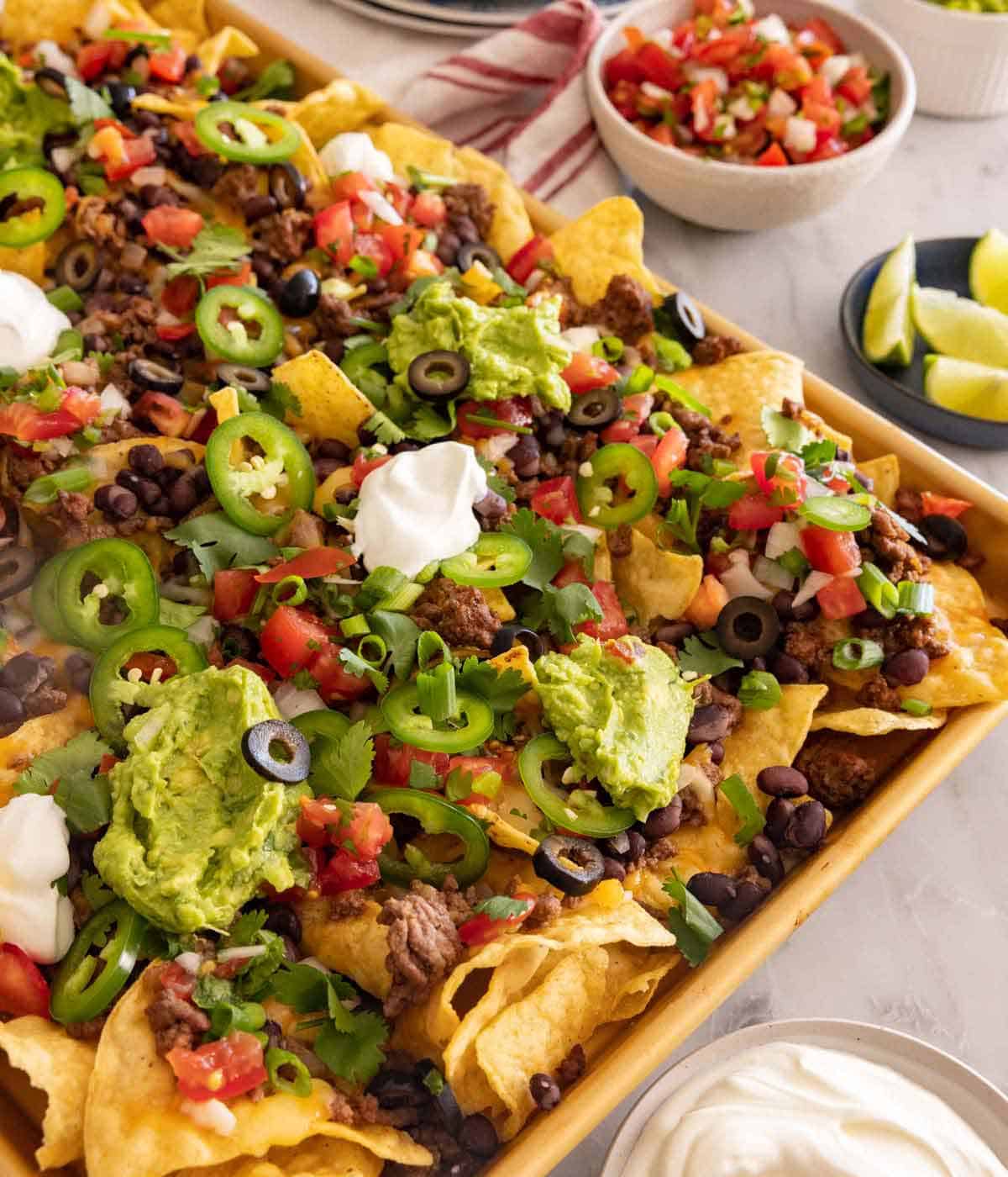 A sheet pan of nachos loaded with toppings with more in bowls around it.