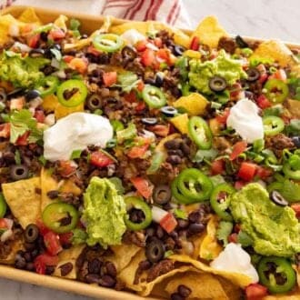 A sheet pan with nachos with assorted toppings.
