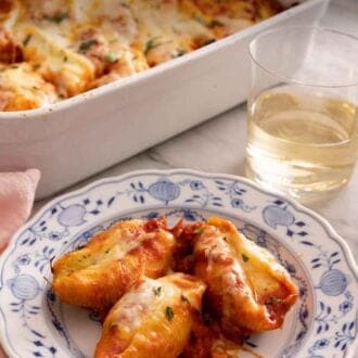 Pinterest graphic of a plate of stuffed shells in front of the baking dish and a glass of wine.