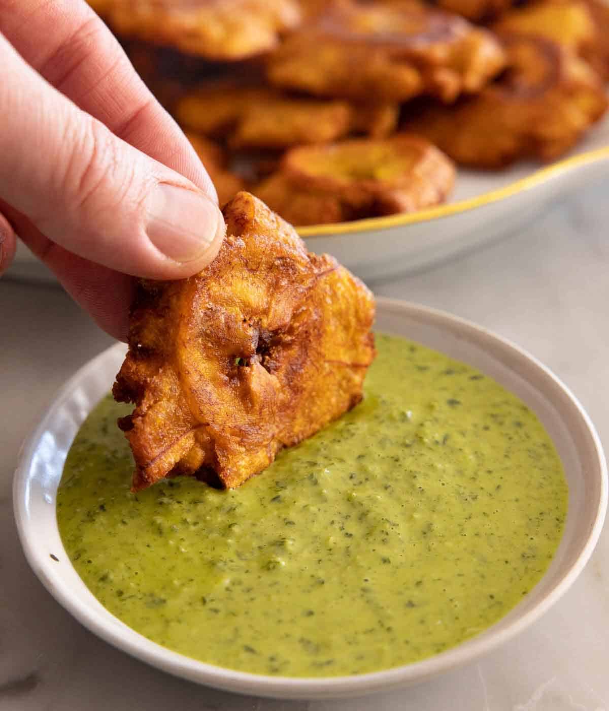 A tostone dipped into a green sauce.