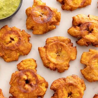 Overhead view of tostones placed in a single layer on a marble surface.