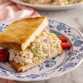A plate with bread filled with tuna salad by a glass of water.