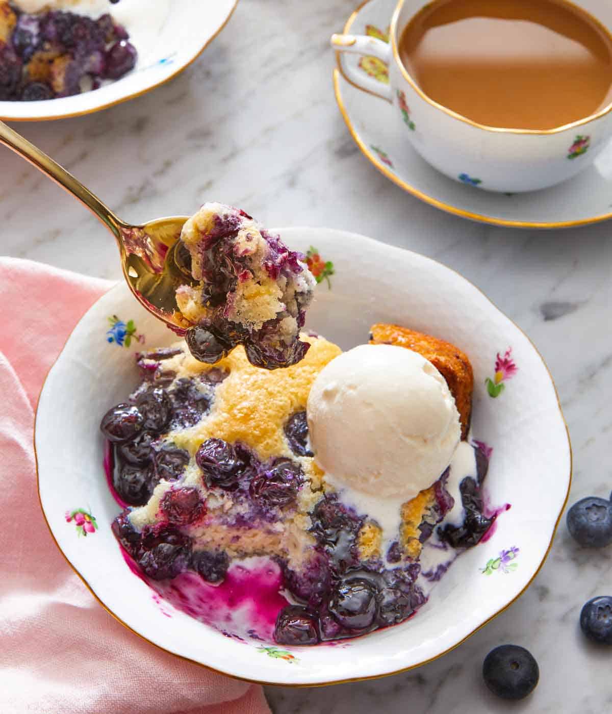 A spoonful of blueberry cobbler lifted from a bowl of cobbler and ice cream.