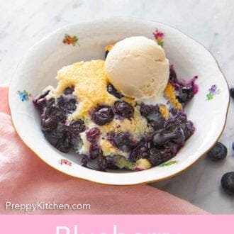 Pinterest graphic of a bowl of blueberry cobbler with a scoop of vanilla ice cream on top.