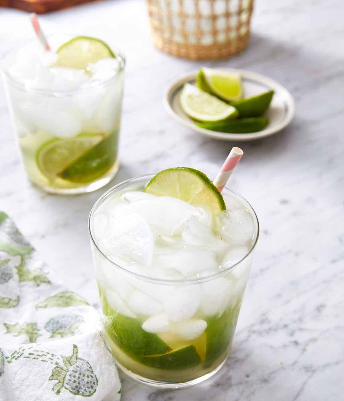 Two glasses of caipirinha with a small plate of cut limes in the background.