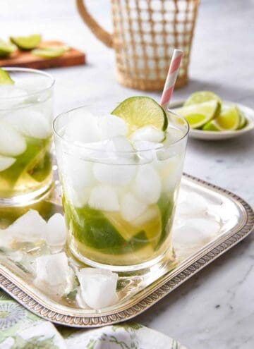A silver tray with two glasses of caipirinha with fresh lime and a straw on top.