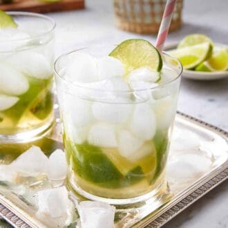 Pinterest graphic of a tray with two glasses of caipirinha with ice scattered around.