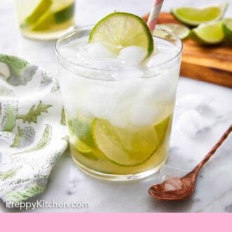 Pinterest graphic of a glass of caipirinha with a fresh lime slice on top. Another glass and more limes in the background.