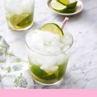 Pinterest graphic of two glasses of caipirinha with a small plate of cut limes in the background.